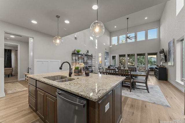 kitchen with sink, a center island with sink, dishwasher, light hardwood / wood-style floors, and hanging light fixtures