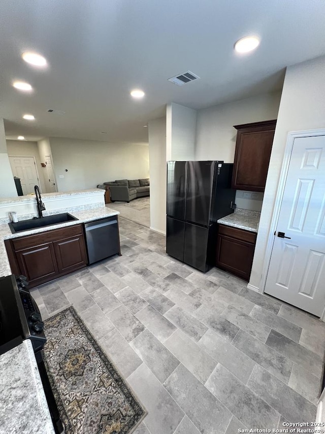 kitchen featuring dishwasher, black fridge, sink, light stone countertops, and dark brown cabinetry