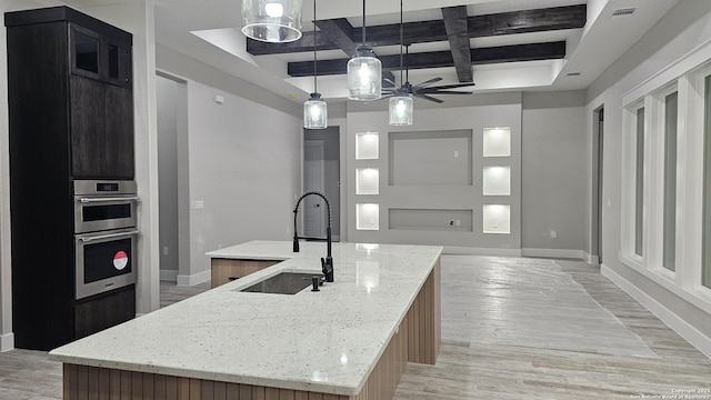 kitchen with decorative light fixtures, sink, coffered ceiling, and a kitchen island with sink