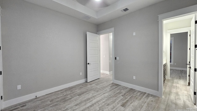 unfurnished bedroom with a raised ceiling and light hardwood / wood-style flooring