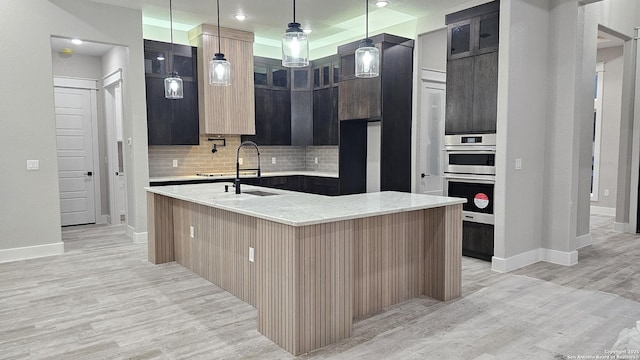 kitchen featuring decorative backsplash, light stone countertops, pendant lighting, and a center island with sink