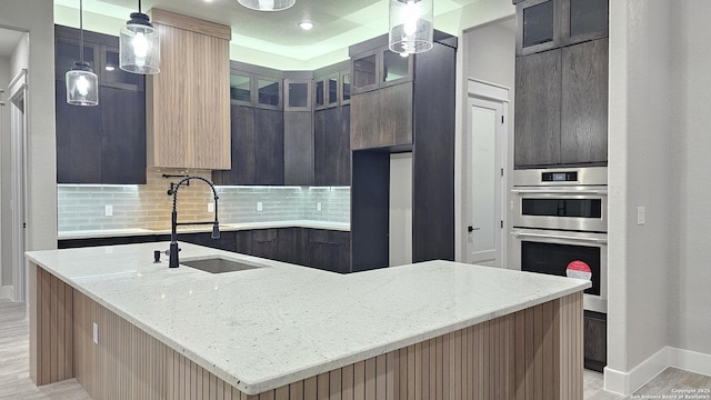 kitchen featuring light stone countertops, decorative light fixtures, tasteful backsplash, sink, and a center island with sink