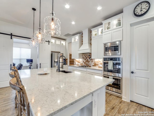 kitchen with premium range hood, white cabinets, a barn door, decorative light fixtures, and stainless steel appliances