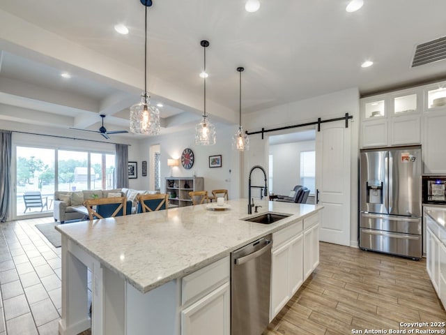 kitchen with appliances with stainless steel finishes, a barn door, an island with sink, and sink