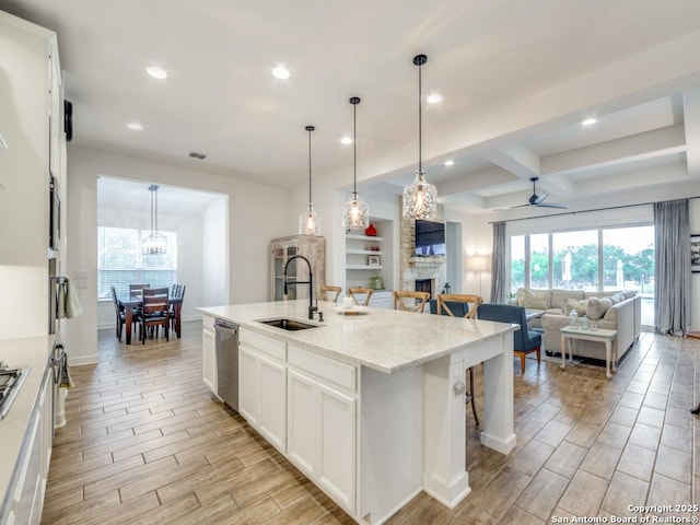 kitchen with a kitchen island with sink, white cabinets, sink, stainless steel dishwasher, and ceiling fan