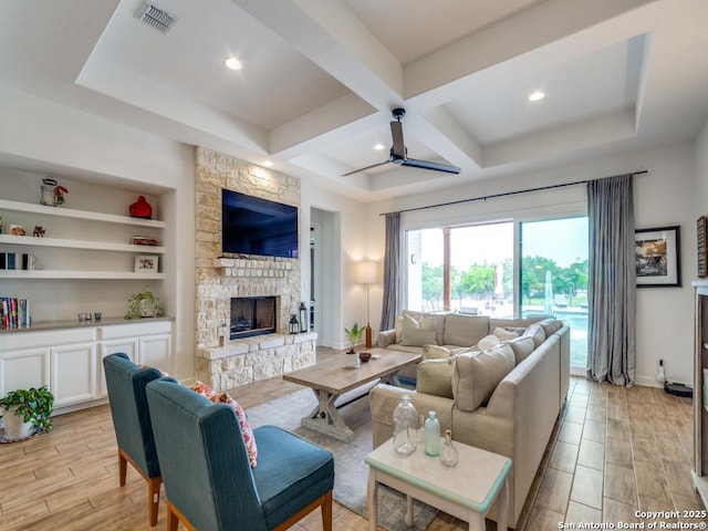 living room featuring coffered ceiling, a stone fireplace, built in shelves, ceiling fan, and beamed ceiling