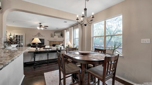 dining space with a fireplace, dark wood-type flooring, and ceiling fan with notable chandelier