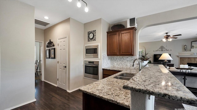 kitchen featuring light stone countertops, appliances with stainless steel finishes, sink, dark hardwood / wood-style floors, and a tiled fireplace