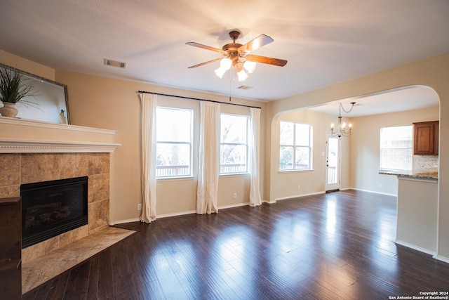 unfurnished living room featuring a tile fireplace, ceiling fan with notable chandelier, and dark wood-type flooring