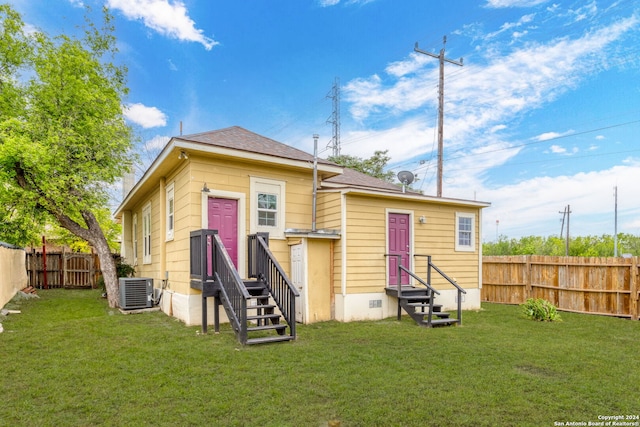 rear view of house featuring central AC unit and a lawn