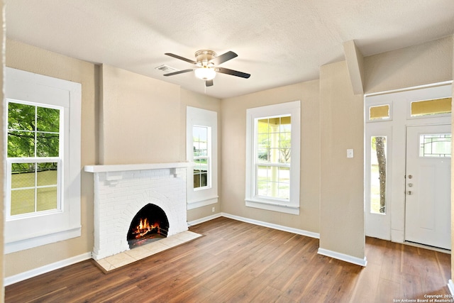 unfurnished living room with hardwood / wood-style flooring, ceiling fan, a textured ceiling, and a brick fireplace