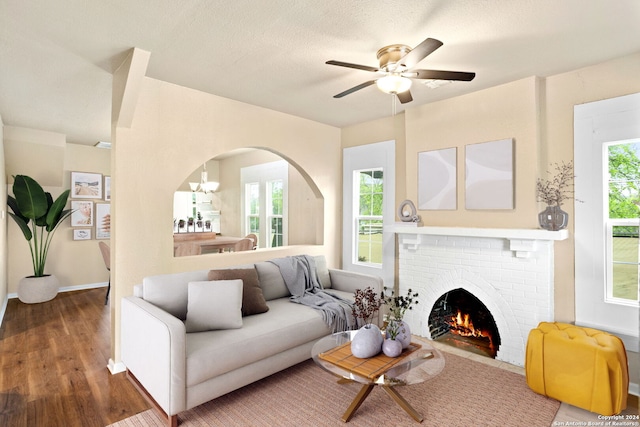 living room featuring plenty of natural light, dark wood-type flooring, ceiling fan with notable chandelier, and a brick fireplace