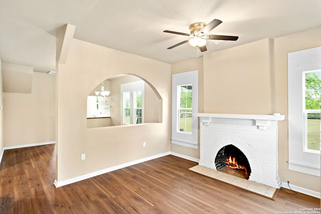 unfurnished living room featuring hardwood / wood-style flooring, ceiling fan with notable chandelier, plenty of natural light, and a fireplace