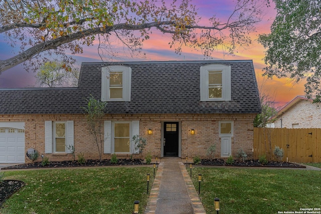 view of property with brick siding, roof with shingles, a front lawn, and fence