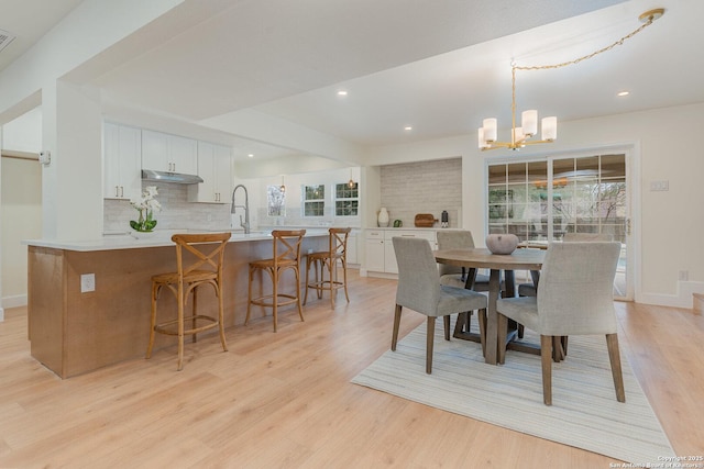 dining space featuring sink, light hardwood / wood-style floors, and an inviting chandelier