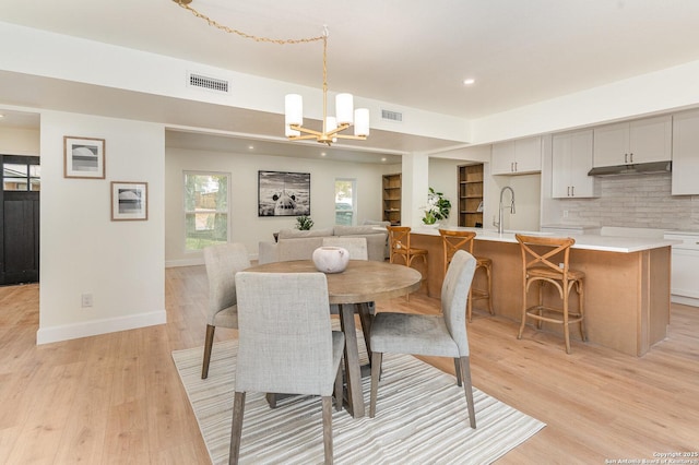 dining area with a notable chandelier, sink, and light hardwood / wood-style flooring