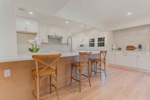 kitchen featuring a kitchen breakfast bar, backsplash, white cabinetry, and a kitchen island with sink