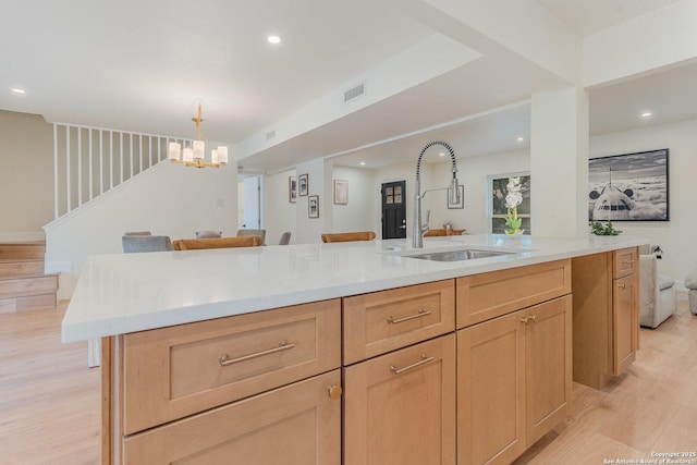 kitchen with light brown cabinets, an island with sink, light hardwood / wood-style floors, and sink