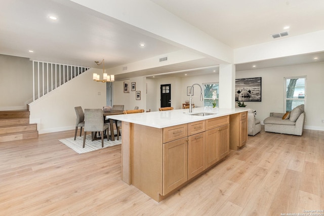 kitchen with sink, hanging light fixtures, an inviting chandelier, light hardwood / wood-style flooring, and a center island with sink