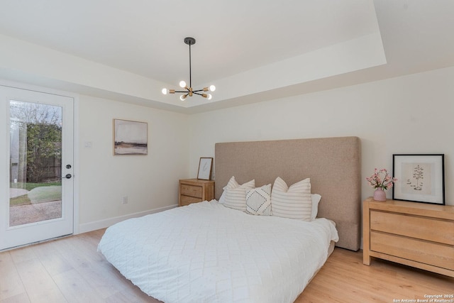 bedroom with a tray ceiling, access to exterior, light hardwood / wood-style flooring, and a chandelier