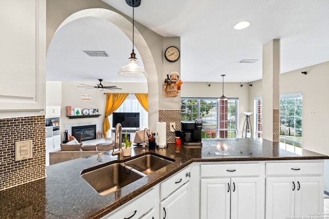 kitchen featuring dark stone countertops, sink, white cabinets, and hanging light fixtures