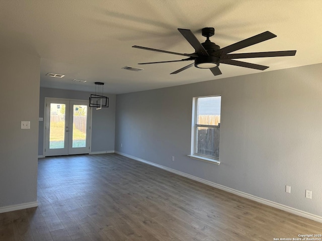 spare room featuring french doors, ceiling fan with notable chandelier, hardwood / wood-style flooring, and a wealth of natural light