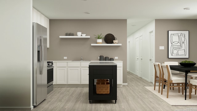 kitchen with stove, white cabinets, sink, stainless steel fridge, and light hardwood / wood-style floors