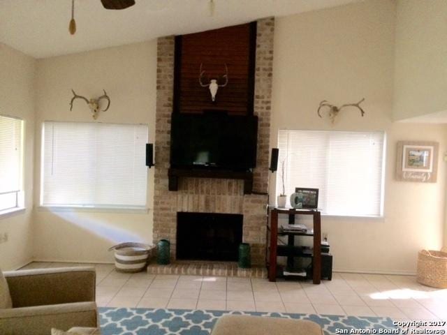 tiled living room with a fireplace, ceiling fan, and lofted ceiling