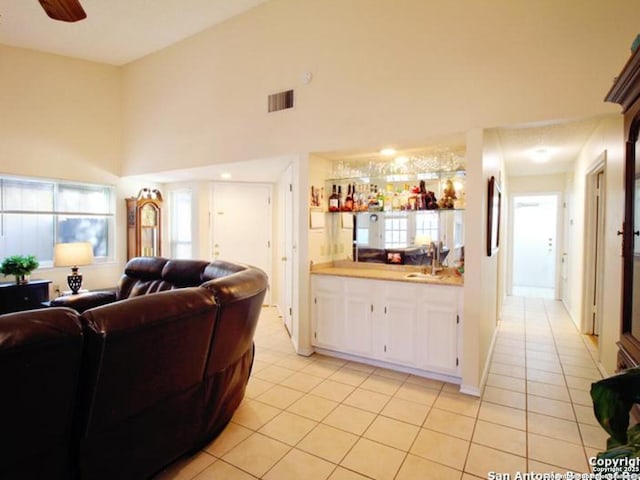 living room with ceiling fan, wet bar, light tile patterned floors, and a high ceiling