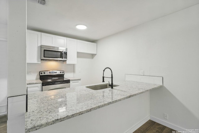 kitchen with kitchen peninsula, light stone counters, stainless steel appliances, sink, and white cabinets