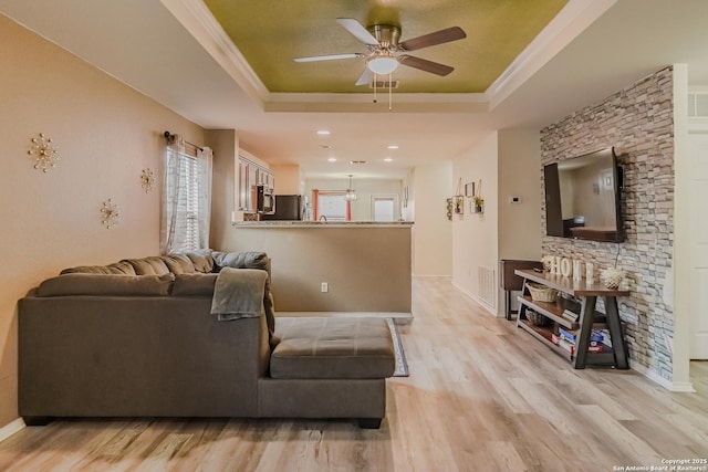 living room featuring ceiling fan, a raised ceiling, ornamental molding, and light hardwood / wood-style flooring