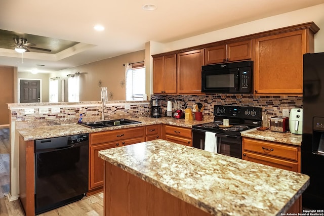 kitchen featuring a raised ceiling, light stone counters, sink, and black appliances