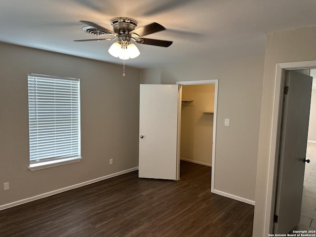 unfurnished bedroom featuring a closet, a spacious closet, ceiling fan, and dark wood-type flooring