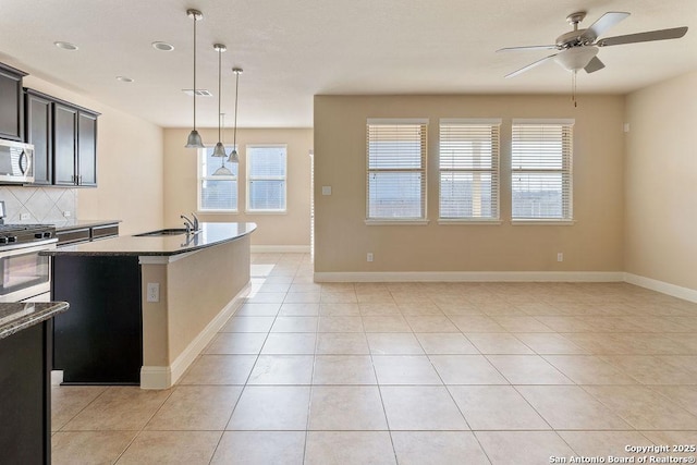 kitchen with appliances with stainless steel finishes, tasteful backsplash, sink, hanging light fixtures, and an island with sink