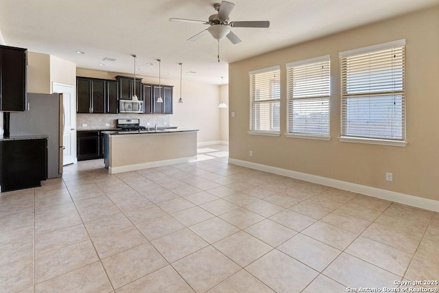 kitchen featuring ceiling fan, an island with sink, decorative backsplash, light tile patterned flooring, and appliances with stainless steel finishes