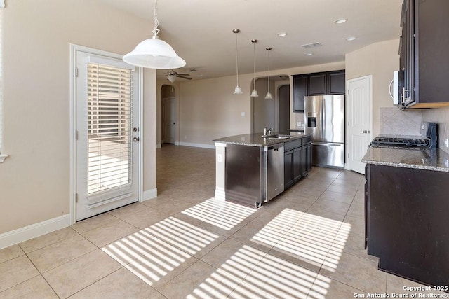 kitchen featuring sink, stainless steel appliances, an island with sink, dark stone counters, and pendant lighting