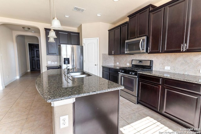 kitchen featuring sink, decorative backsplash, light tile patterned floors, an island with sink, and stainless steel appliances