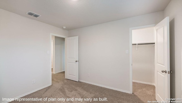 unfurnished bedroom with light colored carpet, a walk in closet, and a closet