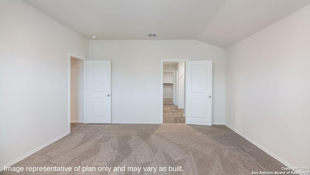 unfurnished bedroom with a walk in closet, light carpet, a closet, and vaulted ceiling