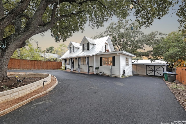 cape cod house featuring covered porch, a garage, and an outbuilding