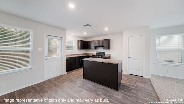 kitchen featuring gas stove, light stone countertops, a center island, dark brown cabinets, and light wood-type flooring