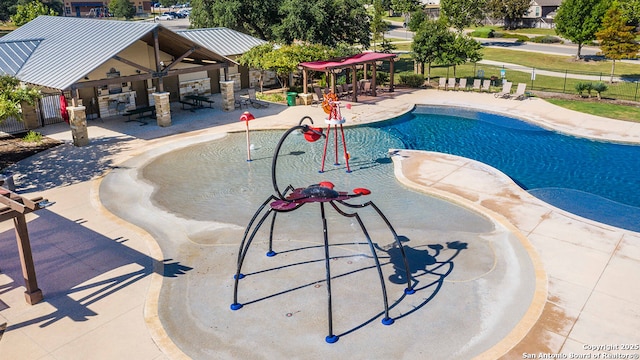 pool with a patio area, a water play area, and fence