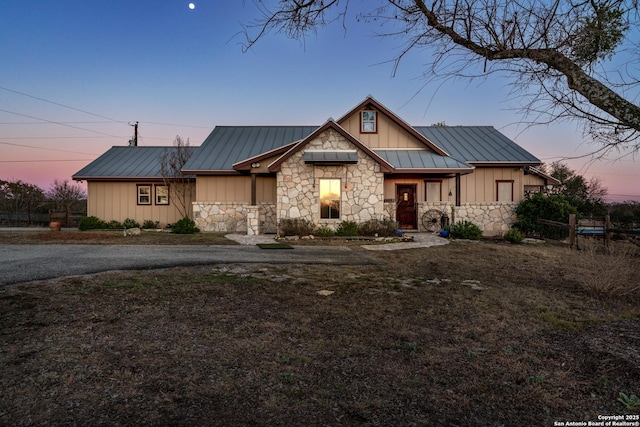 view of front facade featuring fence, a standing seam roof, stone siding, board and batten siding, and metal roof