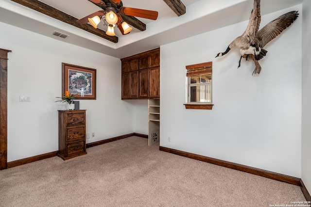 empty room with a raised ceiling, ceiling fan, beam ceiling, and light colored carpet