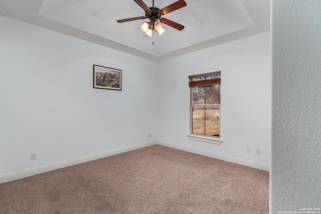 carpeted empty room featuring ceiling fan and a raised ceiling