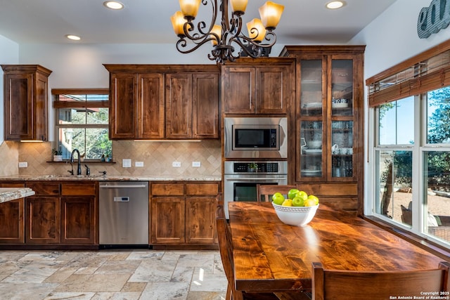 kitchen featuring sink, decorative backsplash, light stone countertops, appliances with stainless steel finishes, and a notable chandelier