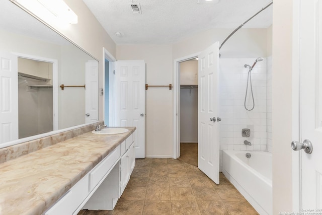 bathroom featuring tile patterned floors, vanity, tiled shower / bath combo, and a textured ceiling