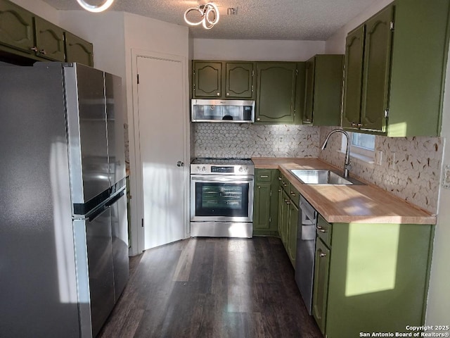 kitchen with appliances with stainless steel finishes, dark hardwood / wood-style floors, sink, green cabinets, and a textured ceiling