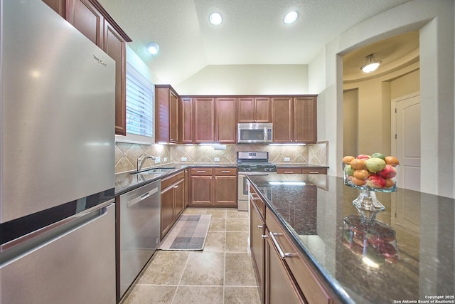 kitchen with lofted ceiling, sink, decorative backsplash, dark stone countertops, and appliances with stainless steel finishes