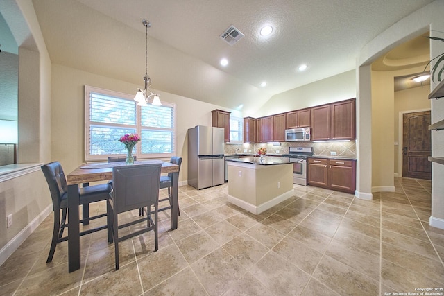 kitchen with decorative backsplash, stainless steel appliances, vaulted ceiling, a notable chandelier, and a center island